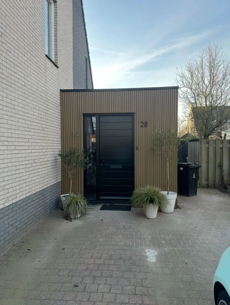 Opgeleverde aanbouw in Breda: nieuwe entree met verticale gevelbekleding, plat dak en een zwarte voordeur met zijlicht