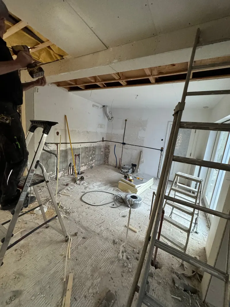 Woningrenovatie in Rotterdam: de wanden zijn tot op de steen gestript, nieuw leidingwerk voor water en elektra ligt op de wand en het plafond is deels open om bij de balklaag te kunnen; op de vloer liggen isolatieplaten met folielaag klaar