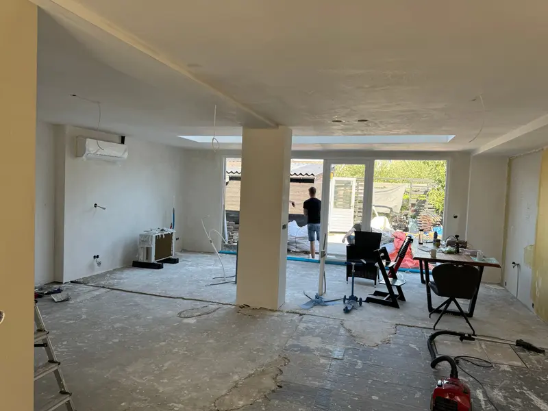 Doorgebroken begane grond in Etten-Leur met een ingepakte kolom midden in de ruimte, lichtkoepels in het nieuwe plafond, gestucte wanden en een pui naar de tuin; de vloer ligt nog open