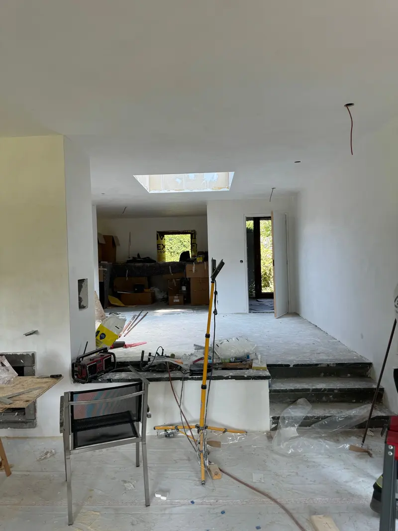 Woning in Rotterdam na het stukadoors- en schilderwerk: wanden en plafond zijn glad afgewerkt, een langwerpige lichtstraat brengt daglicht tot in het midden van de woning en een paar treden met donkere stenen afdekking verbindt twee vloerniveaus; verderop staat de keuken nog in dozen