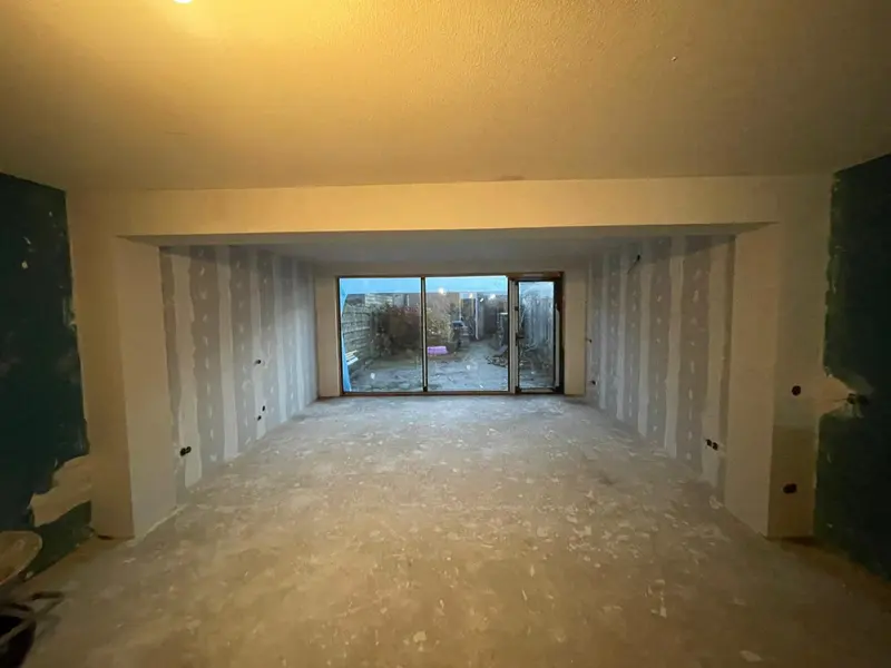 Doorgang van de bestaande woning naar de nieuwe uitbouw in Breda: boven de opening is de constructie ingepakt, de wanden in de uitbouw staan in gipsplaat en achterin zit de schuifpui naar de tuin