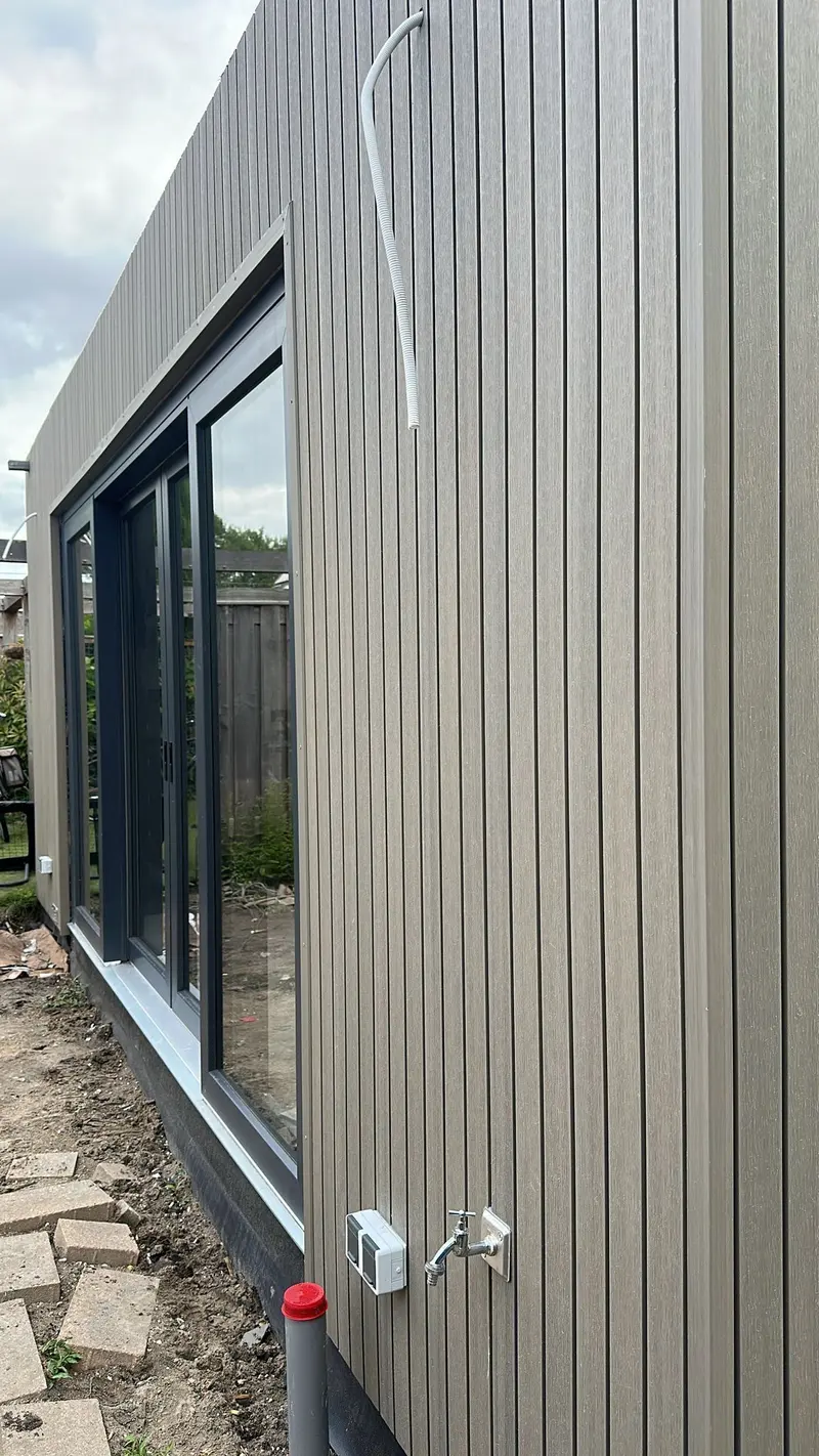 Opgeleverde uitbouw in Breda: verticale gevelbekleding, antracietkleurige schuifpui over de volle breedte en een buitenkraan met wandcontactdoos