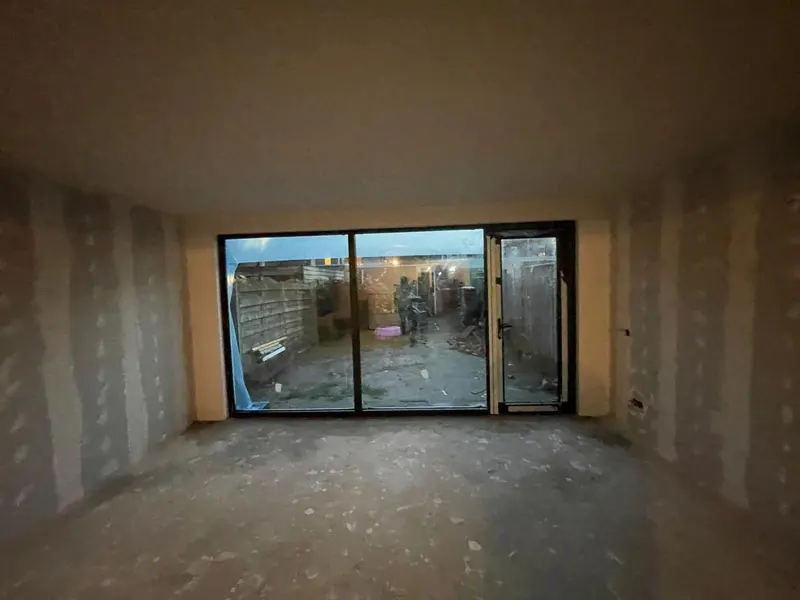 Uitbouw in Breda aan het eind van de dag: gipsplaatwanden met gevulde naden en een zwarte schuifpui met zijdeur naar de tuin