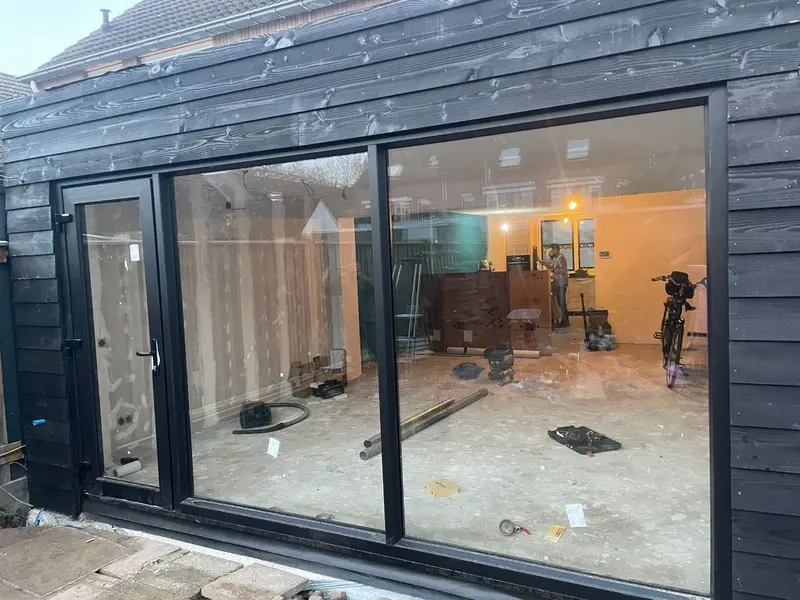 Schuifpui van een uitbouw in Breda in zwart gebeitste gevelbekleding; binnen staan de wanden nog in de ruwbouw en ligt de vloer open