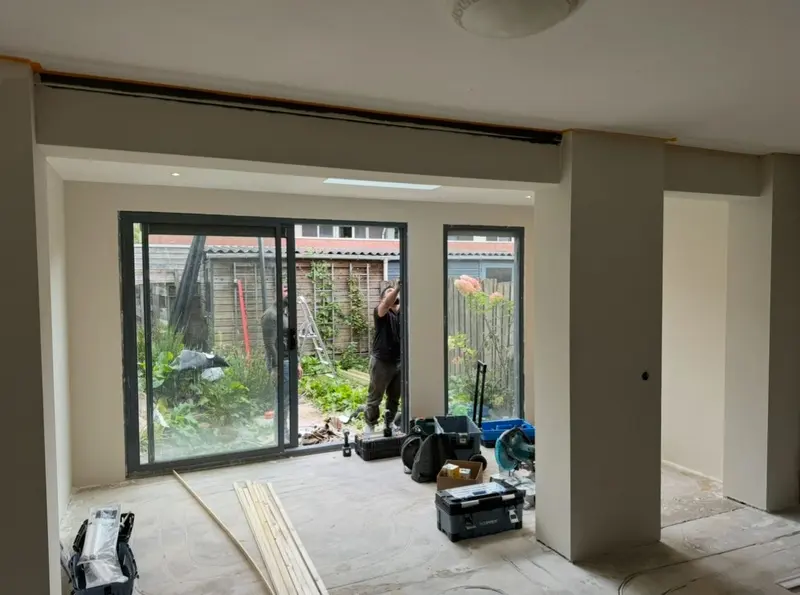 Opgeleverde uitbouw in Etten-Leur, gezien vanuit de woonkamer: gestucte wanden en plafond met inbouwspots, antracietkleurige schuifpui met zijraam en een daklicht dat extra daglicht binnenbrengt