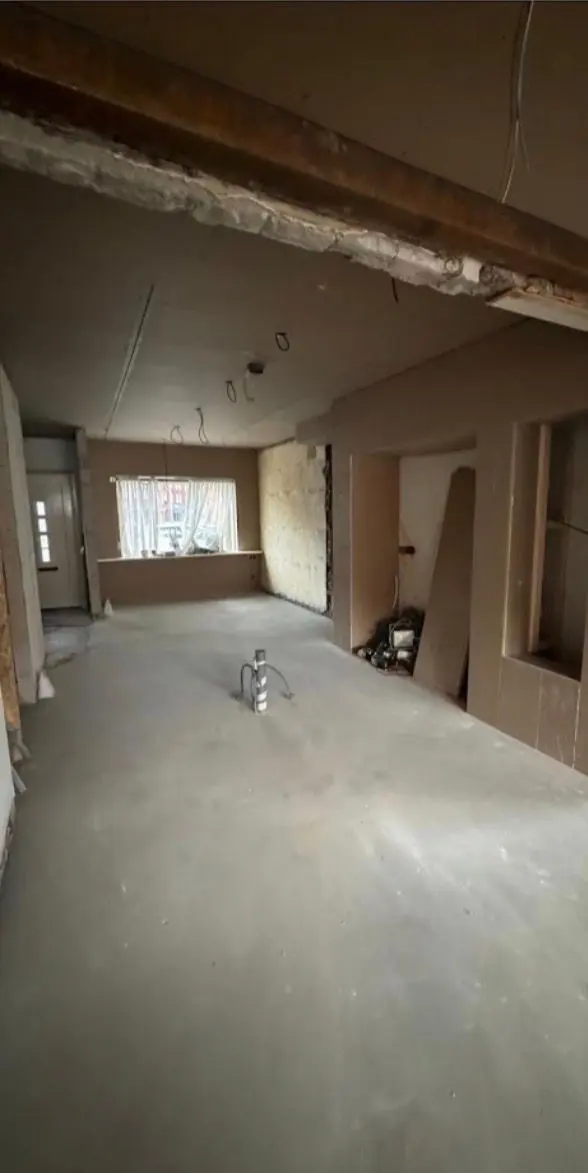 Dezelfde woning in de ruwbouwfase: de dragende scheidingswand is verwijderd en de opening is over de volle breedte afgevangen door een ligger, de nieuwe vloer is gestort, de wanden staan in de ruwbouw met uitgespaarde nissen en uit het plafond hangen de elektraleidingen